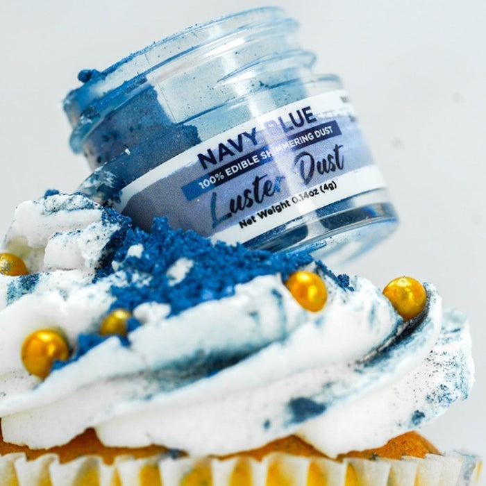 Navy blue edible luster dust spilling from a jar onto a white-frosted cupcake with gold sprinkles.