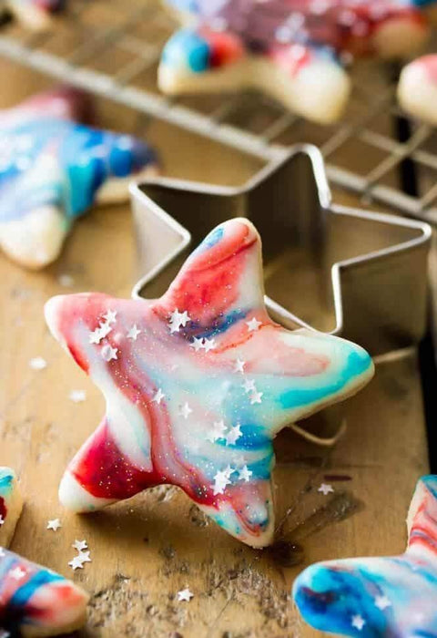 Star-shaped sugar cookie with red, white, and blue marbled icing, topped with tiny white star sprinkles.