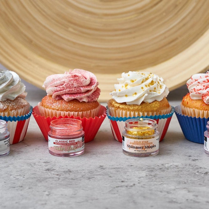 Four festive cupcakes with silver, pink, gold, and red edible glitter and sprinkles, alongside matching jars.