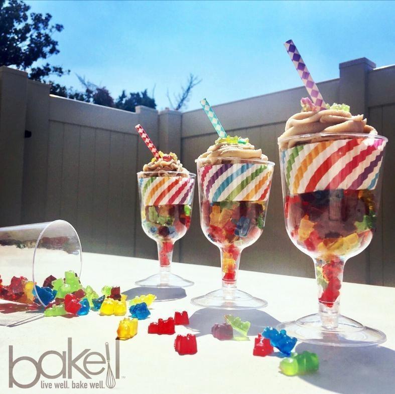 Three colorful gummy bear parfaits with whipped topping and striped straws, set outdoors.