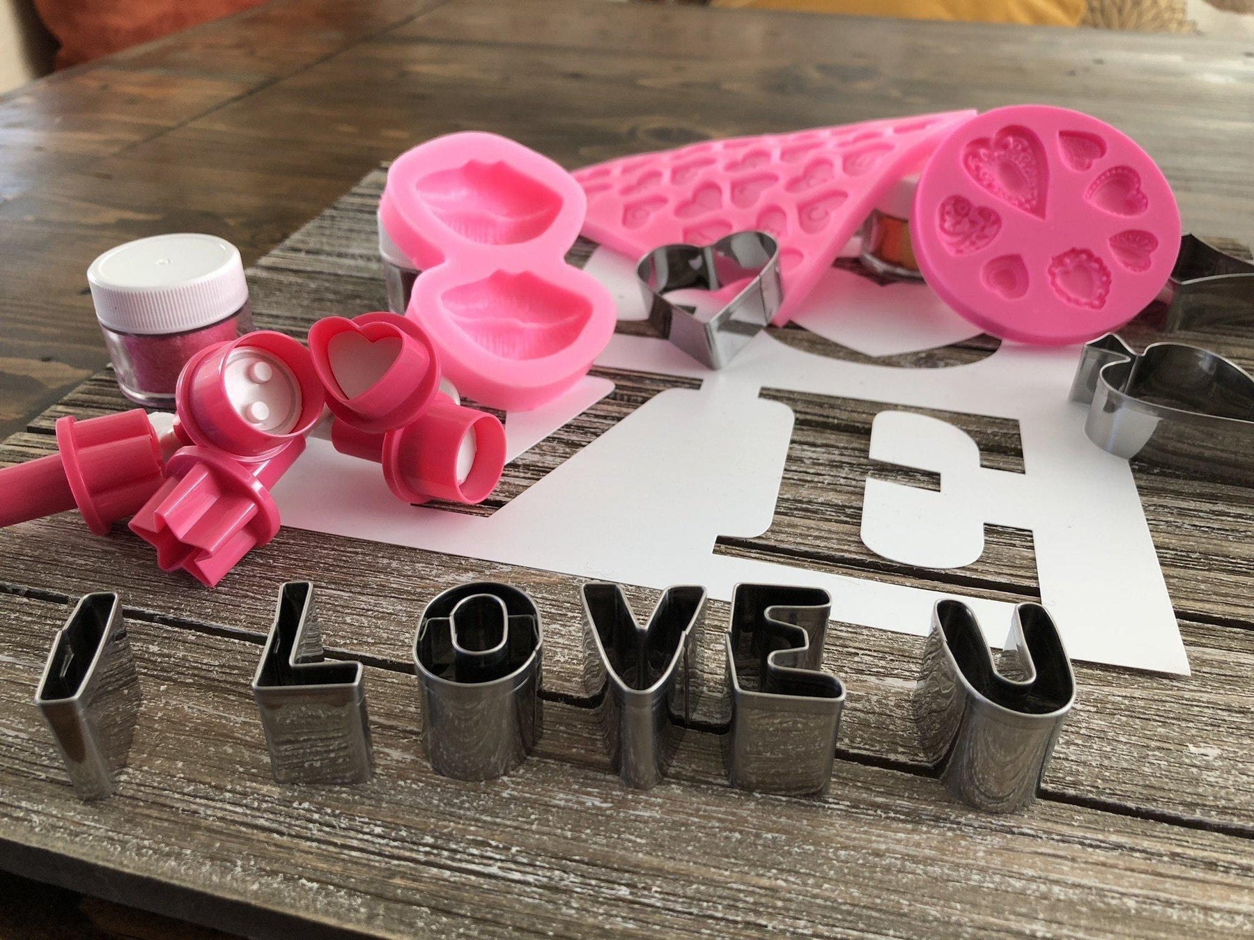 Pink silicone molds, heart cookie cutters, and "I LOVE U" metal letters for baking.