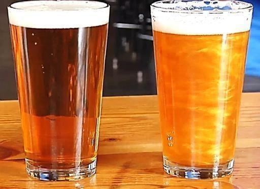 Two pint glasses of beer on a wooden bar, one dark amber and one shimmering golden.