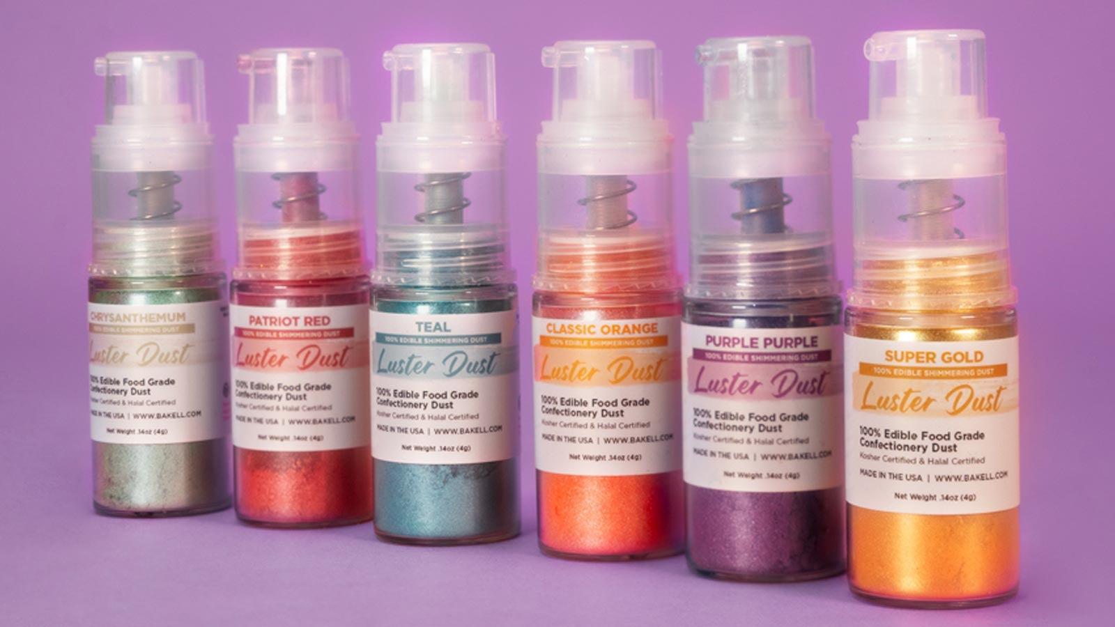 Six bottles of edible luster dust in various shimmery colors: green, red, teal, orange, purple, and gold.