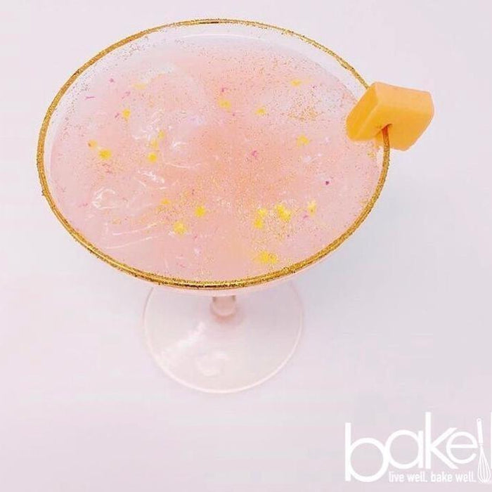Pink cocktail with gold glitter rim, yellow sprinkles, and a mango garnish.