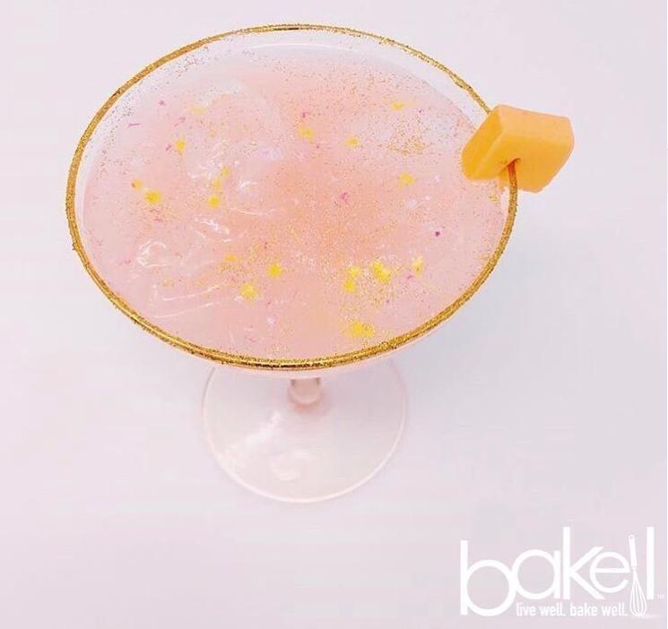 Pink cocktail with gold glitter rim, yellow sprinkles, and a mango garnish.