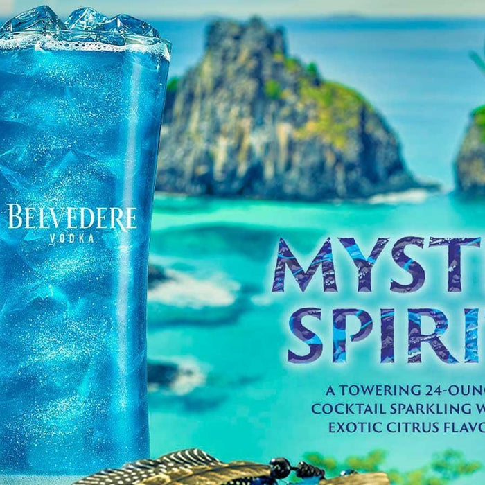 Tall blue Belvedere Vodka "Mystic Spirit" cocktail with ice, set against a tropical island and turquoise ocean.