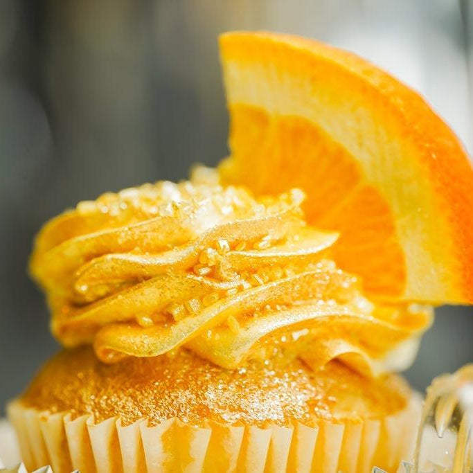 Golden orange cupcake with swirled frosting, sprinkles, and a fresh orange slice.