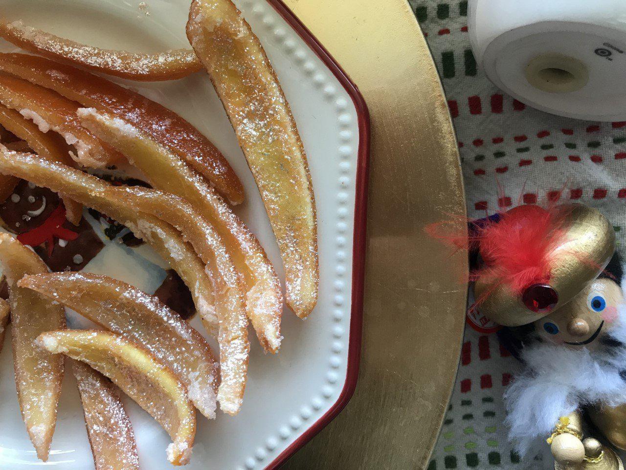 Candied orange peels dusted with powdered sugar on a white plate with a festive nutcracker.