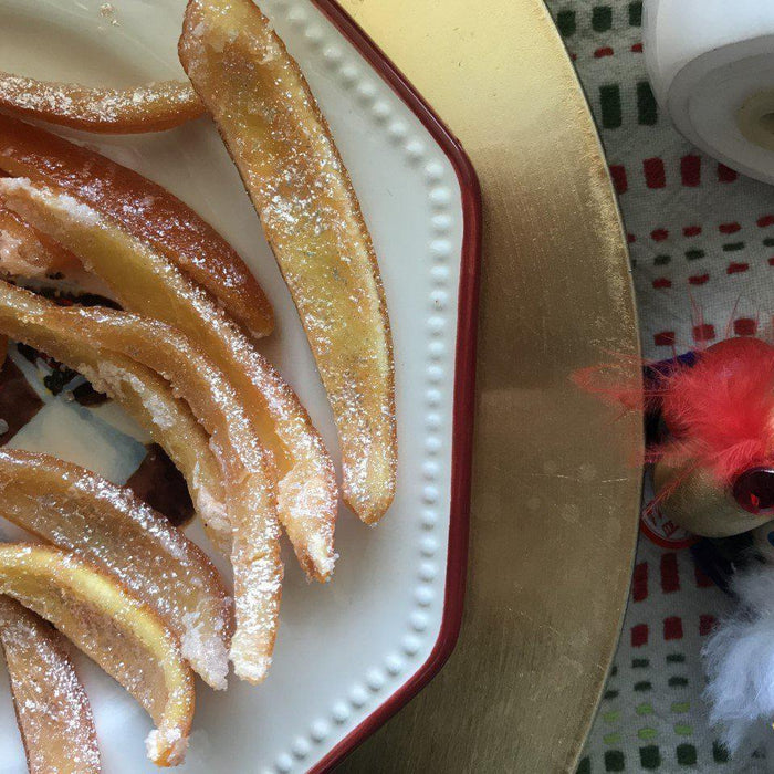 Candied orange peels dusted with powdered sugar on a white plate with a festive nutcracker.