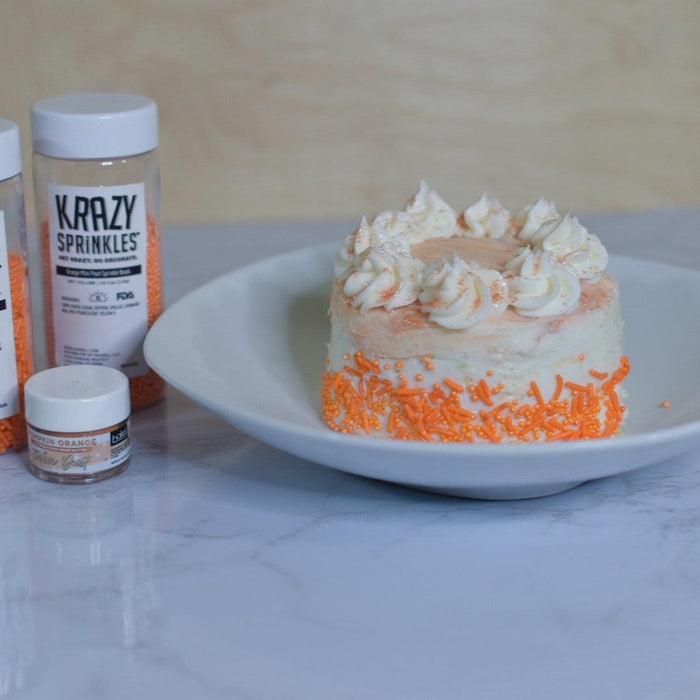 Mini orange cake with white frosting and orange sprinkles, next to Krazy Sprinkles bottles.
