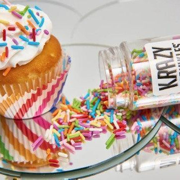 Vanilla cupcake with white frosting and colorful sprinkles next to an overturned bottle of "Krazy Sprinkles.