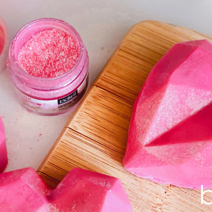 Pink geometric heart-shaped chocolates with edible glitter on a wooden board.