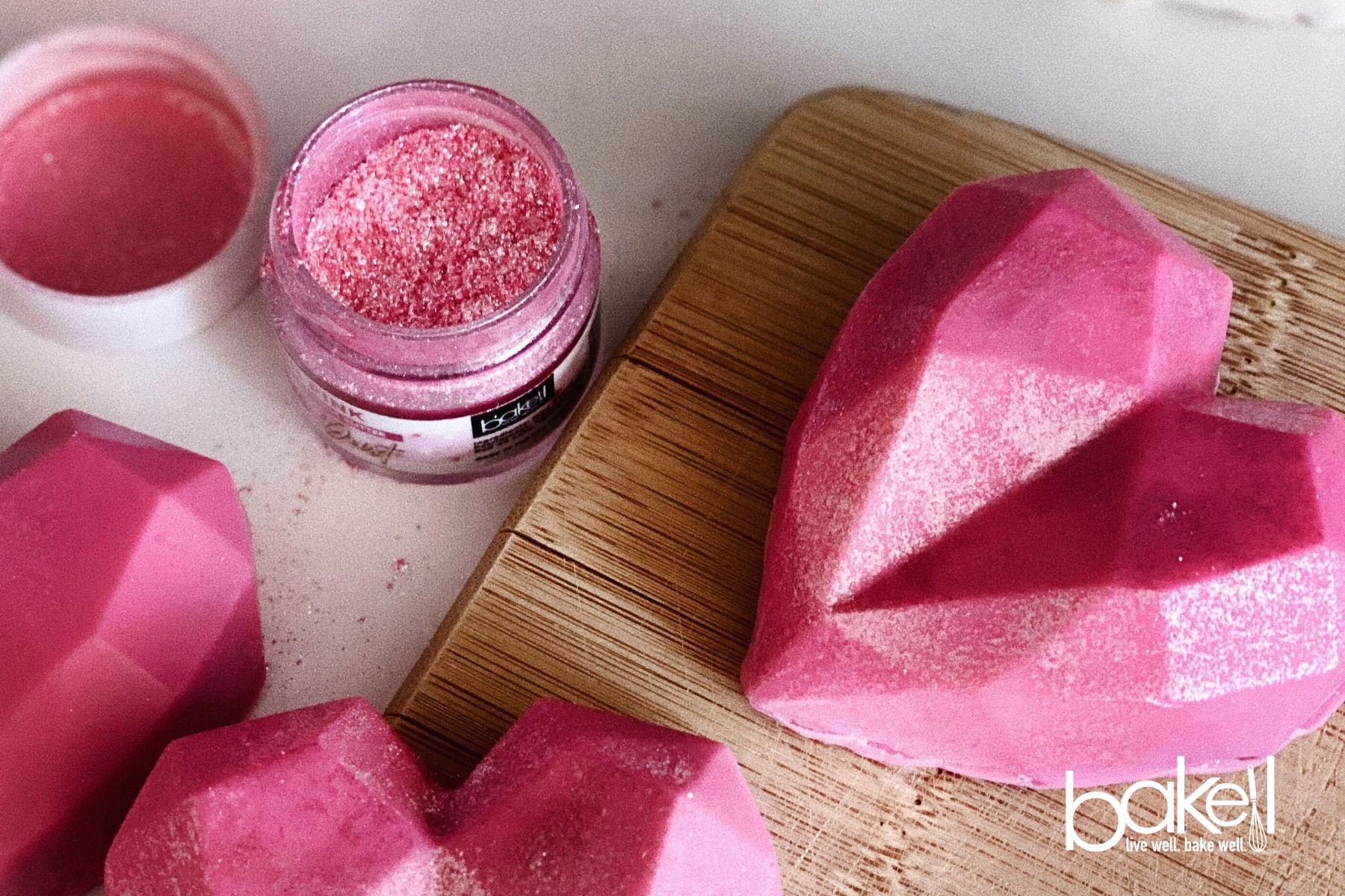 Pink geometric heart-shaped chocolates with edible glitter and a jar of Bakell edible glitter.