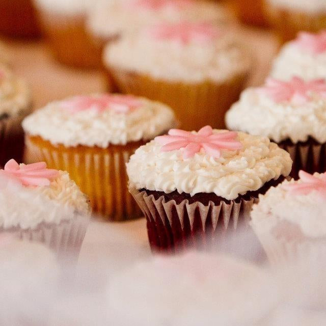Rows of festive cupcakes with white frosting and pink flower decorations.