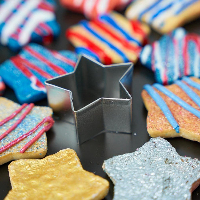 Star-shaped sugar cookies with red, white, and blue icing and sprinkles, surrounding a metal cookie cutter.