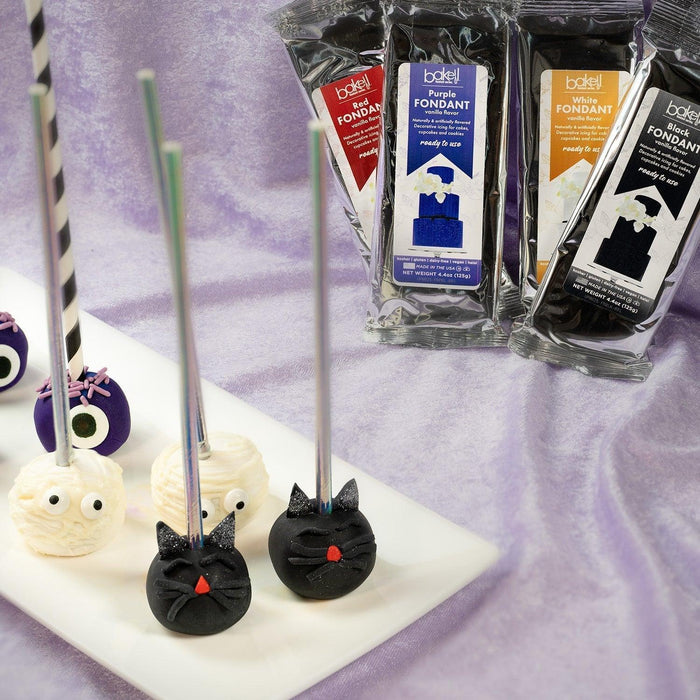Halloween cake pops shaped like black cats and monsters, with colorful fondant packets in the background.
