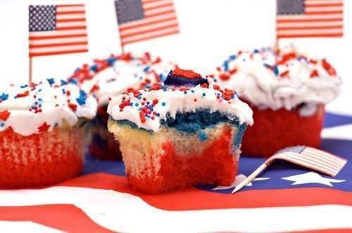Patriotic red, white, and blue cupcakes with sprinkles and American flag toothpicks on a flag tablecloth.