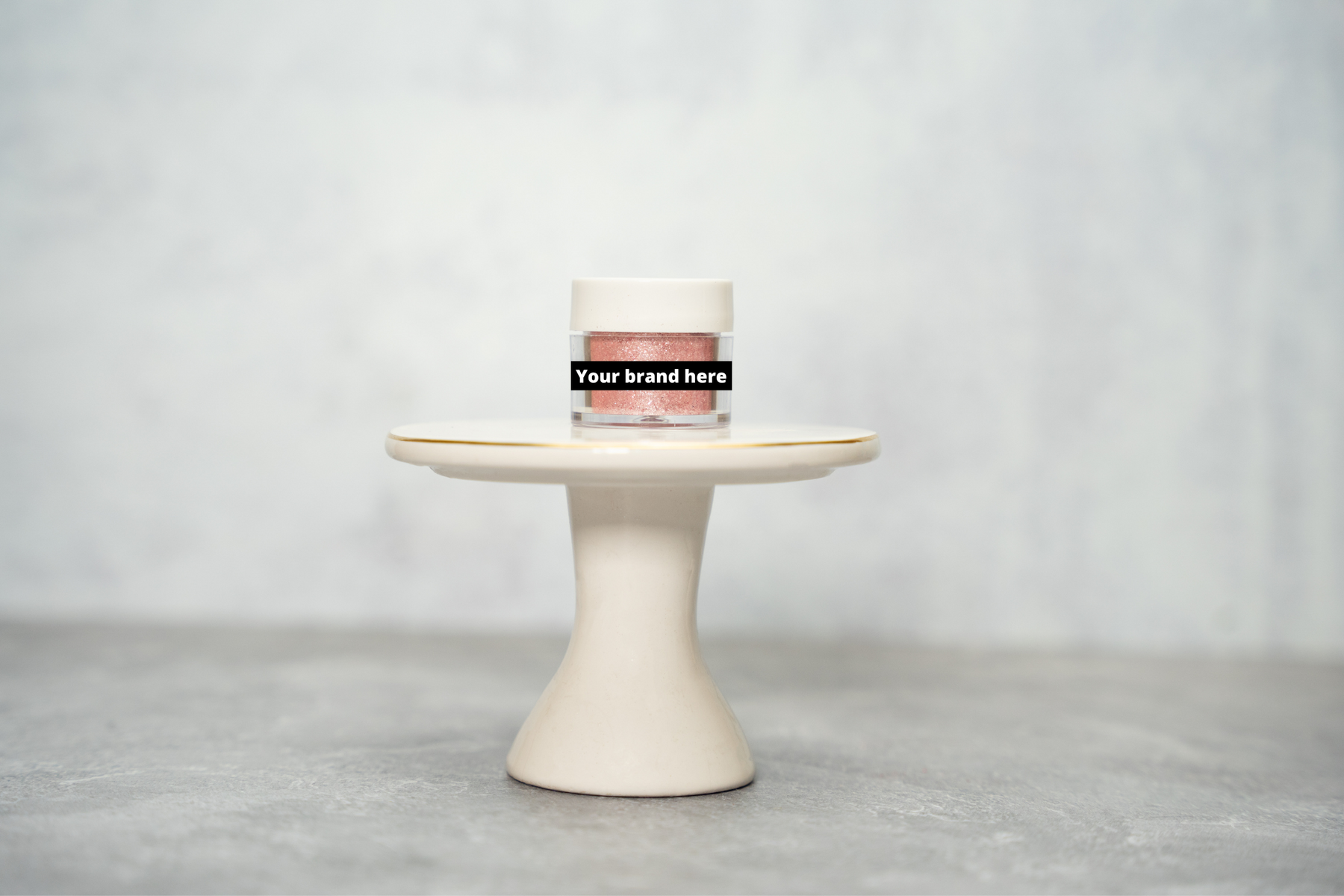 Pink glitter powder in a clear jar with a white lid, displayed on a small white pedestal.