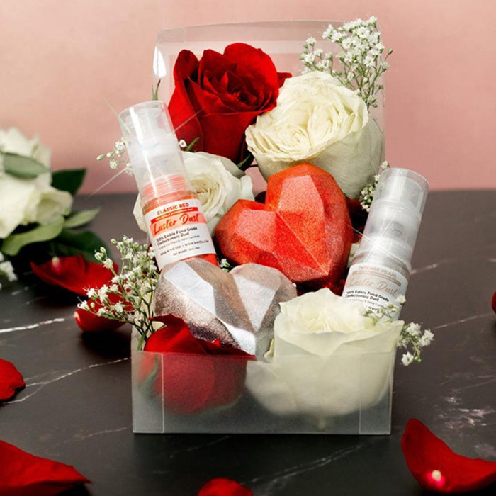 A clear box with red and white roses, two heart-shaped chocolates, and two glitter spray bottles.