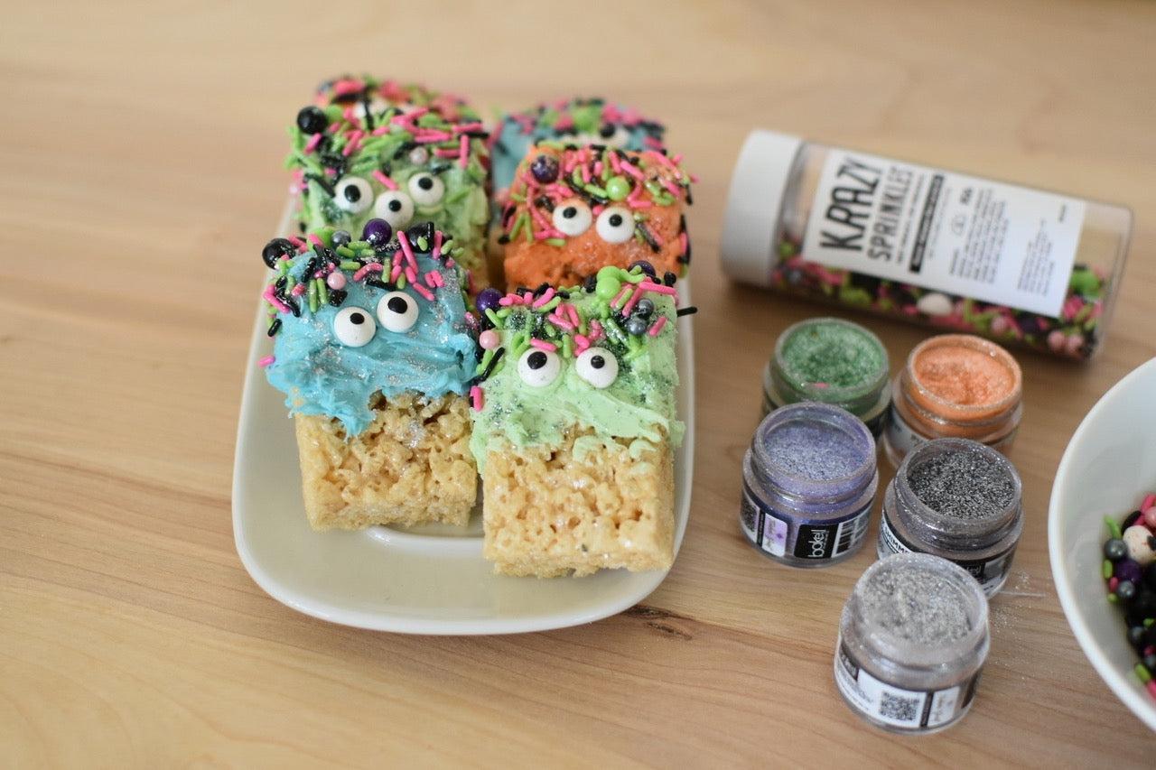 Colorful monster-themed Rice Krispie treats with candy eyes and sprinkles, next to edible glitter jars.