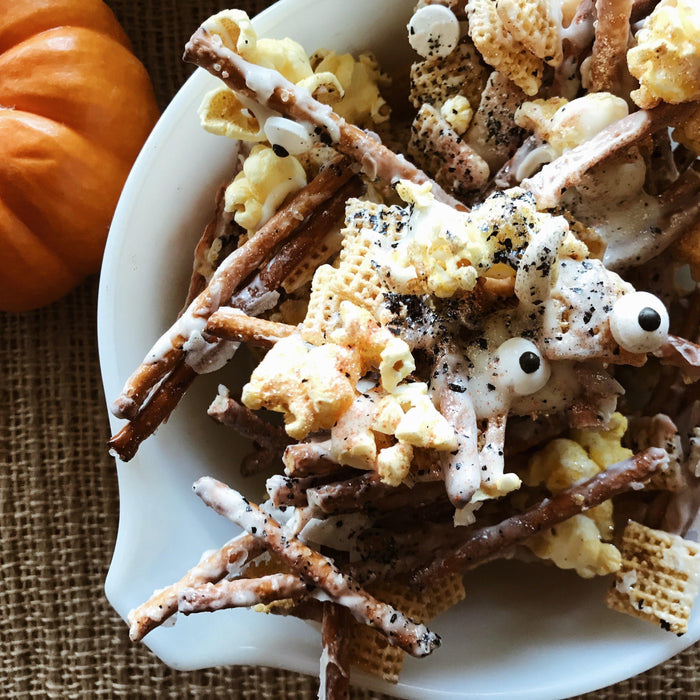 White bowl of Halloween monster munch mix with pretzels, popcorn, cereal, candy eyes, and a pumpkin.