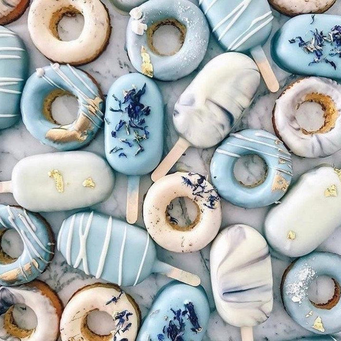 Assortment of light blue and white donuts and cake pops with gold leaf and dried flowers.