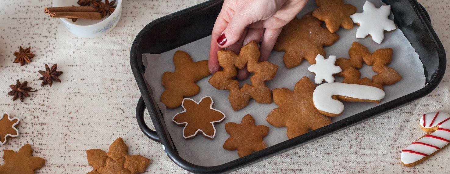 Hand placing a snowflake gingerbread cookie onto a baking sheet with other festive cookies.