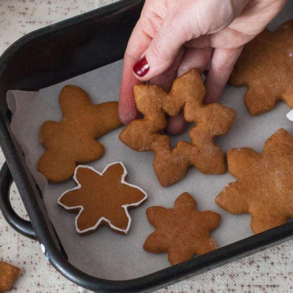 Hand placing a snowflake gingerbread cookie onto a baking sheet with other festive cookies.