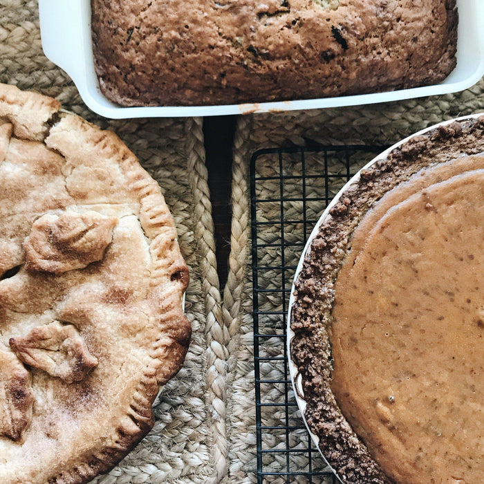 Overhead view of a golden-brown apple pie, pumpkin pie, and banana bread on a woven mat.