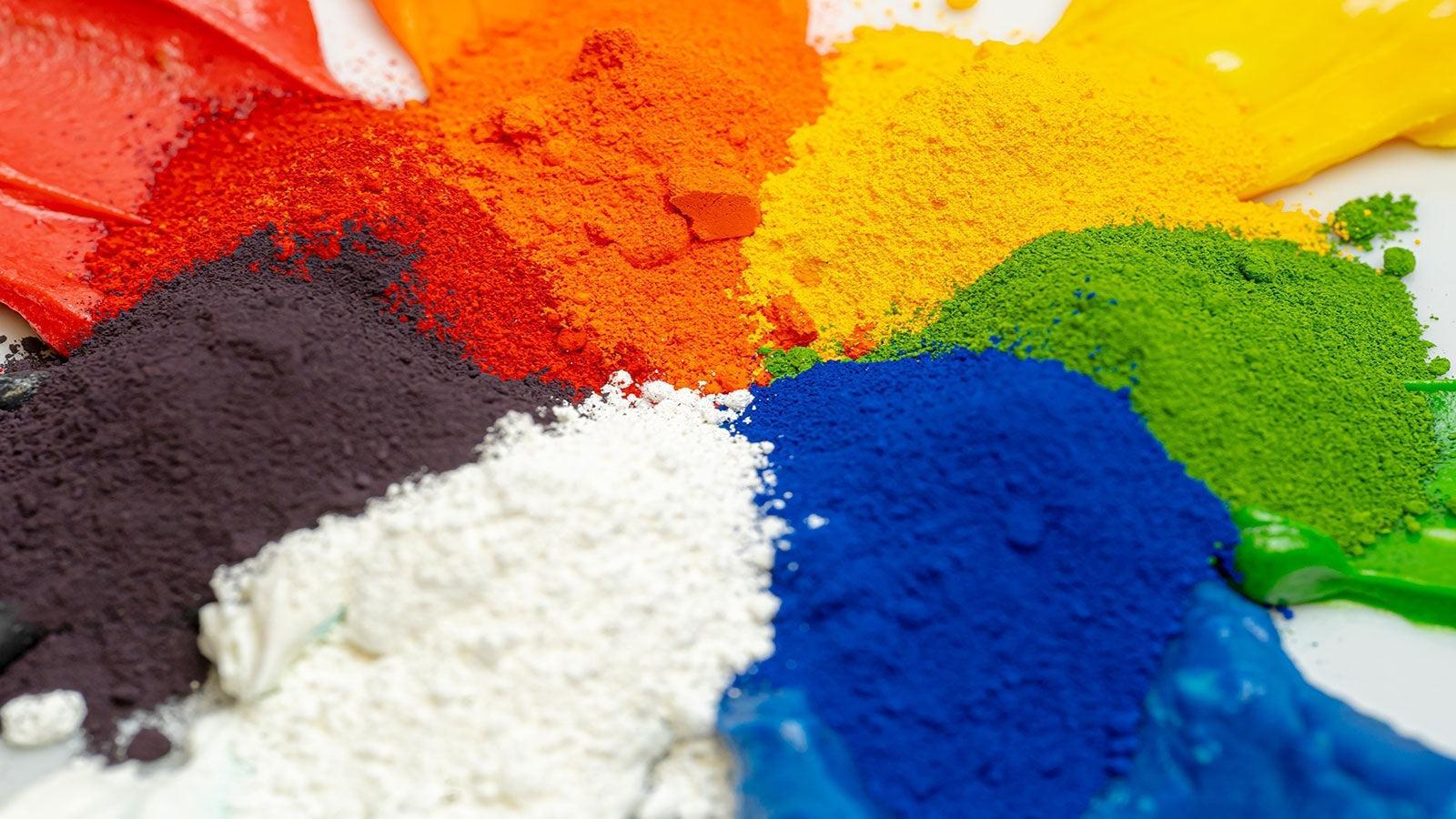Vibrant piles of powdered pigments in red, orange, yellow, green, blue, black, and white.