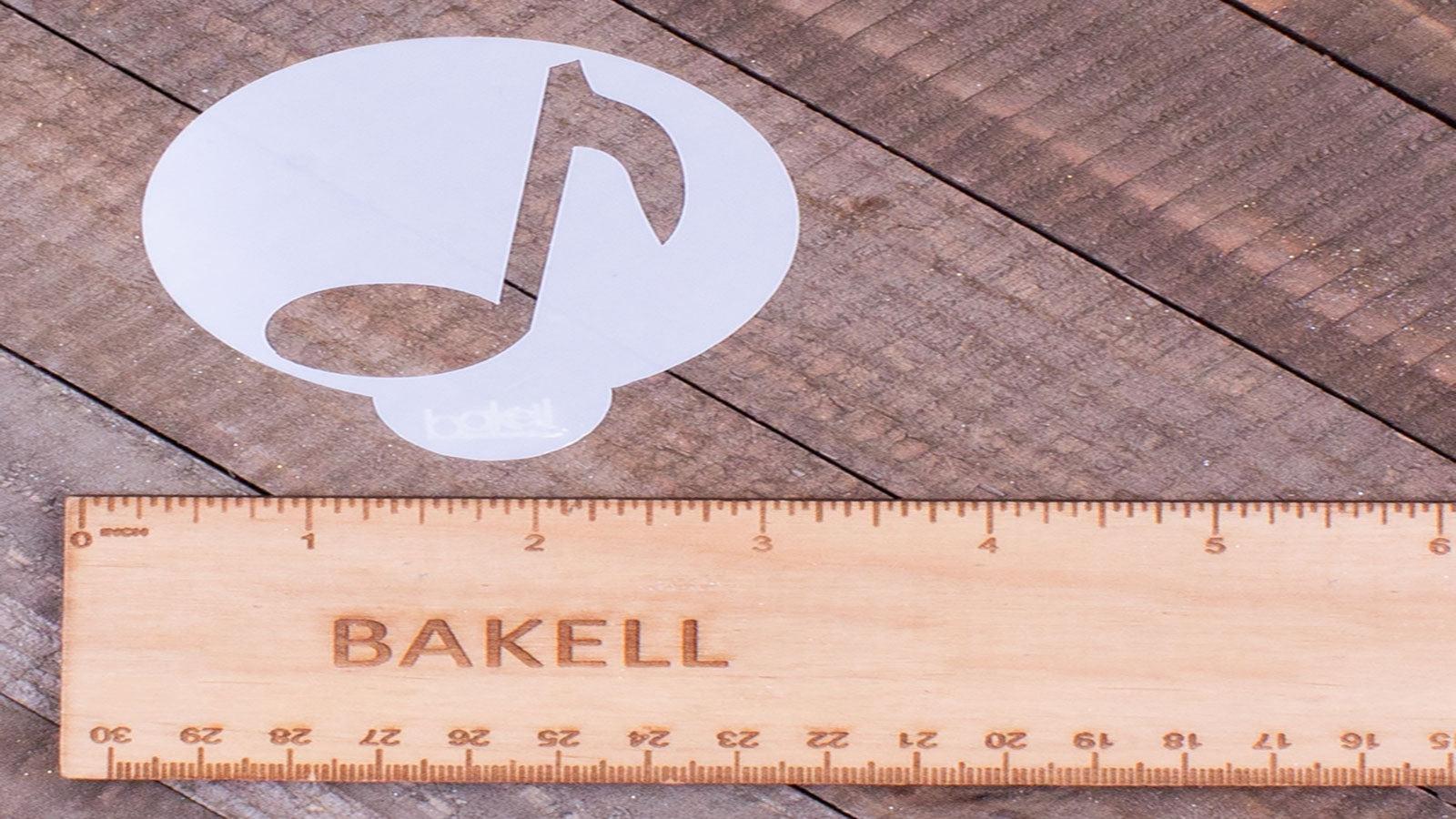 White musical note stencil next to a wooden Bakell ruler on a rustic wood surface.