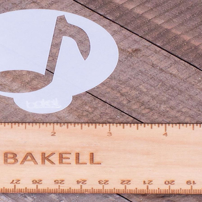 White musical note stencil next to a wooden Bakell ruler on a rustic wood surface.