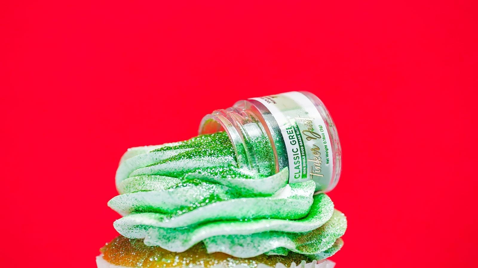 Green edible glitter spilling from a "Tinker Dust" jar onto a frosted cupcake.