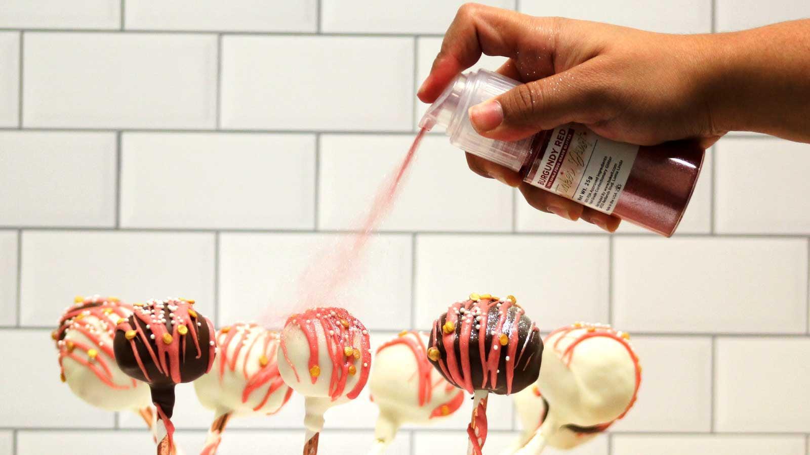 Hand dusting burgundy red edible glitter onto chocolate and white cake pops.