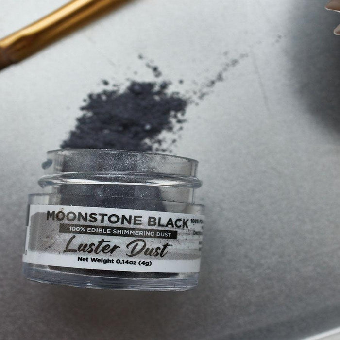 Moonstone Black edible luster dust in a clear jar, with a brush and cupcake liner on a silver tray.