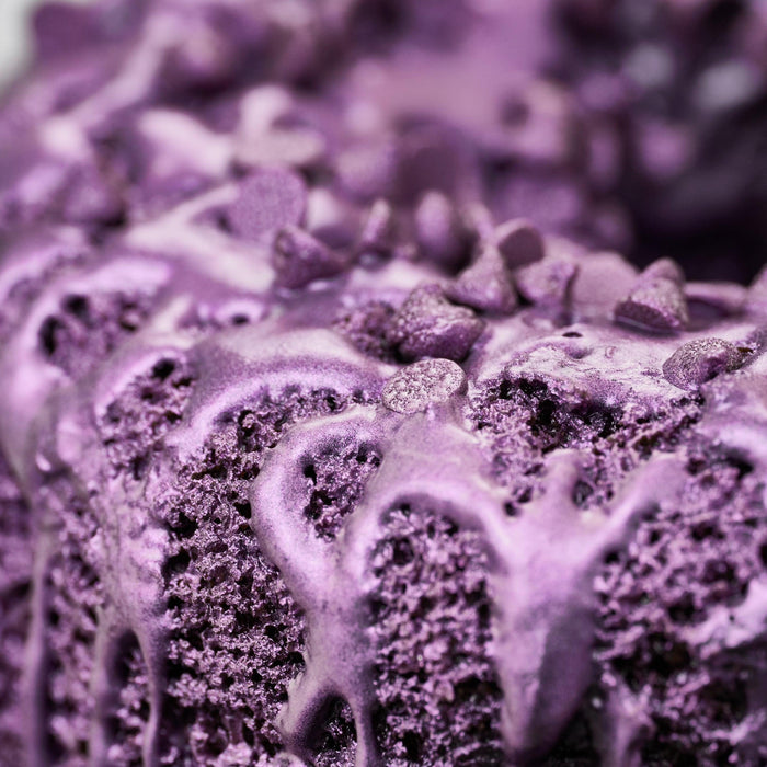 Close-up of a vibrant purple bundt cake with shiny glaze and sprinkles.
