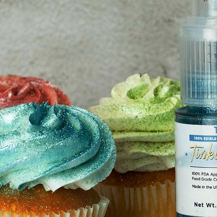 Teal, red, and green glitter-dusted cupcakes next to a bottle of Teal Tinker Dust edible glitter.