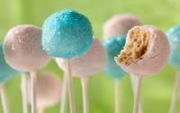 Assortment of pastel pink and blue cake pops, one with a bite taken out, revealing the cake inside.
