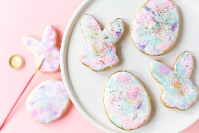 Pastel watercolor Easter bunny and egg cookies with gold accents on a white plate.