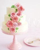 Elegant three-tier white wedding cake adorned with cascading pink sugar roses and green leaves.