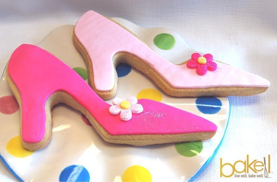 Two high heel shoe cookies, one bright pink and one light pink, decorated with small flowers.
