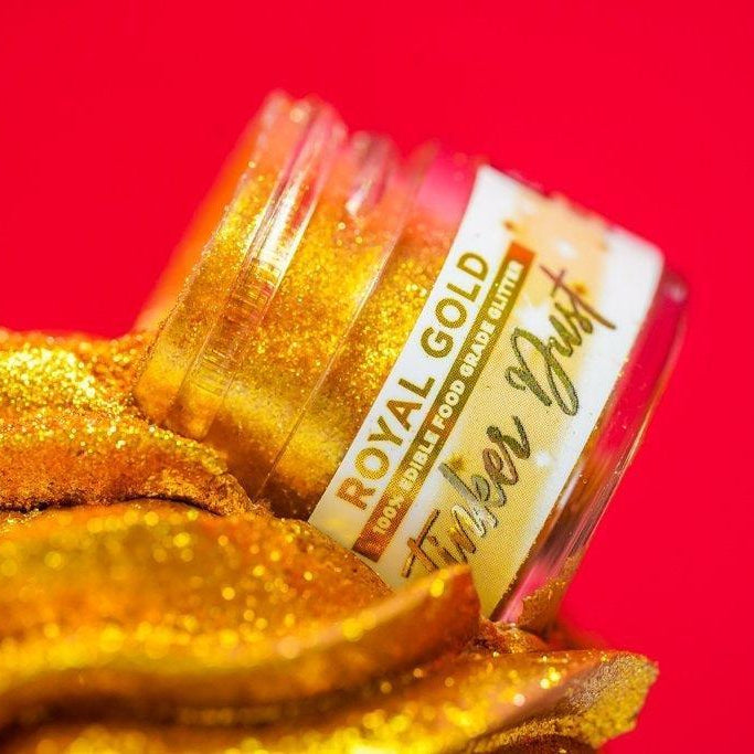 Open jar of Royal Gold edible food-grade glitter, spilling shimmering golden dust onto a red surface.