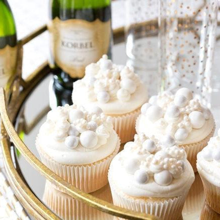 White frosted cupcakes with silver and white candy pearls, served with Korbel champagne on a gold tray.