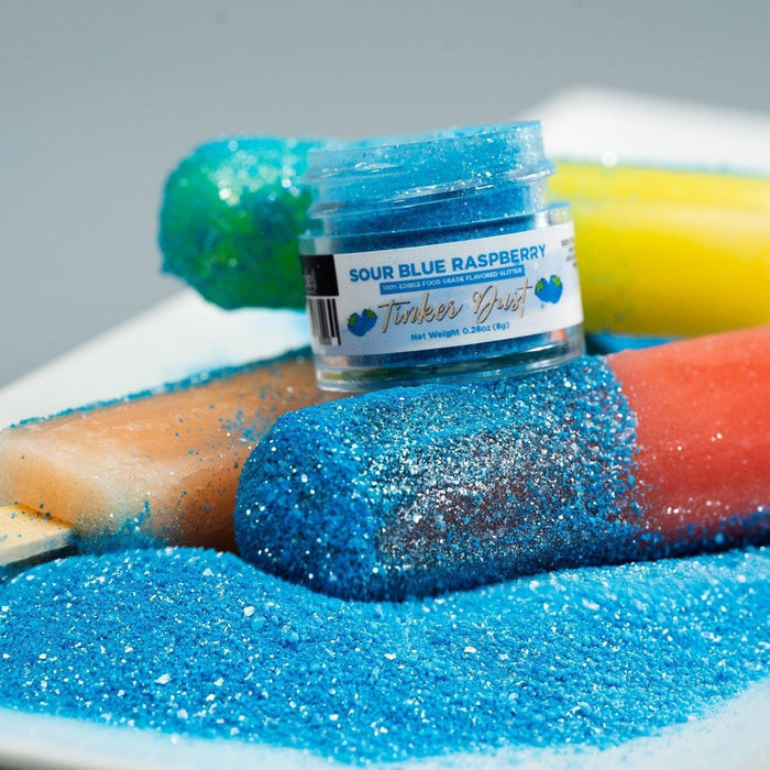 Blue raspberry edible glitter on popsicles with a jar of "Sour Blue Raspberry Tinker Dust.
