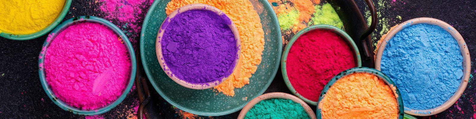 Vibrant bowls of colorful Holi powder in purple, pink, red, blue, yellow, orange, and green.