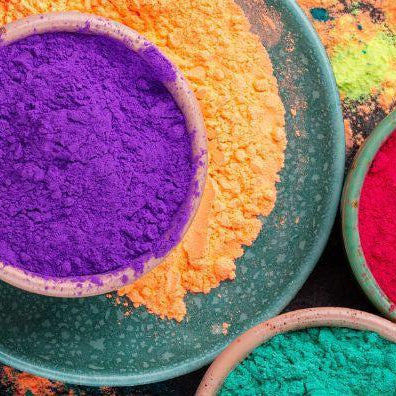 Vibrant bowls of colorful Holi powder in purple, pink, red, blue, yellow, orange, and green.