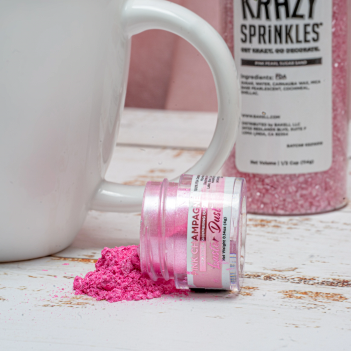 Pink shimmer dust spilled from a small jar next to a white mug and a bottle of pink sprinkles.