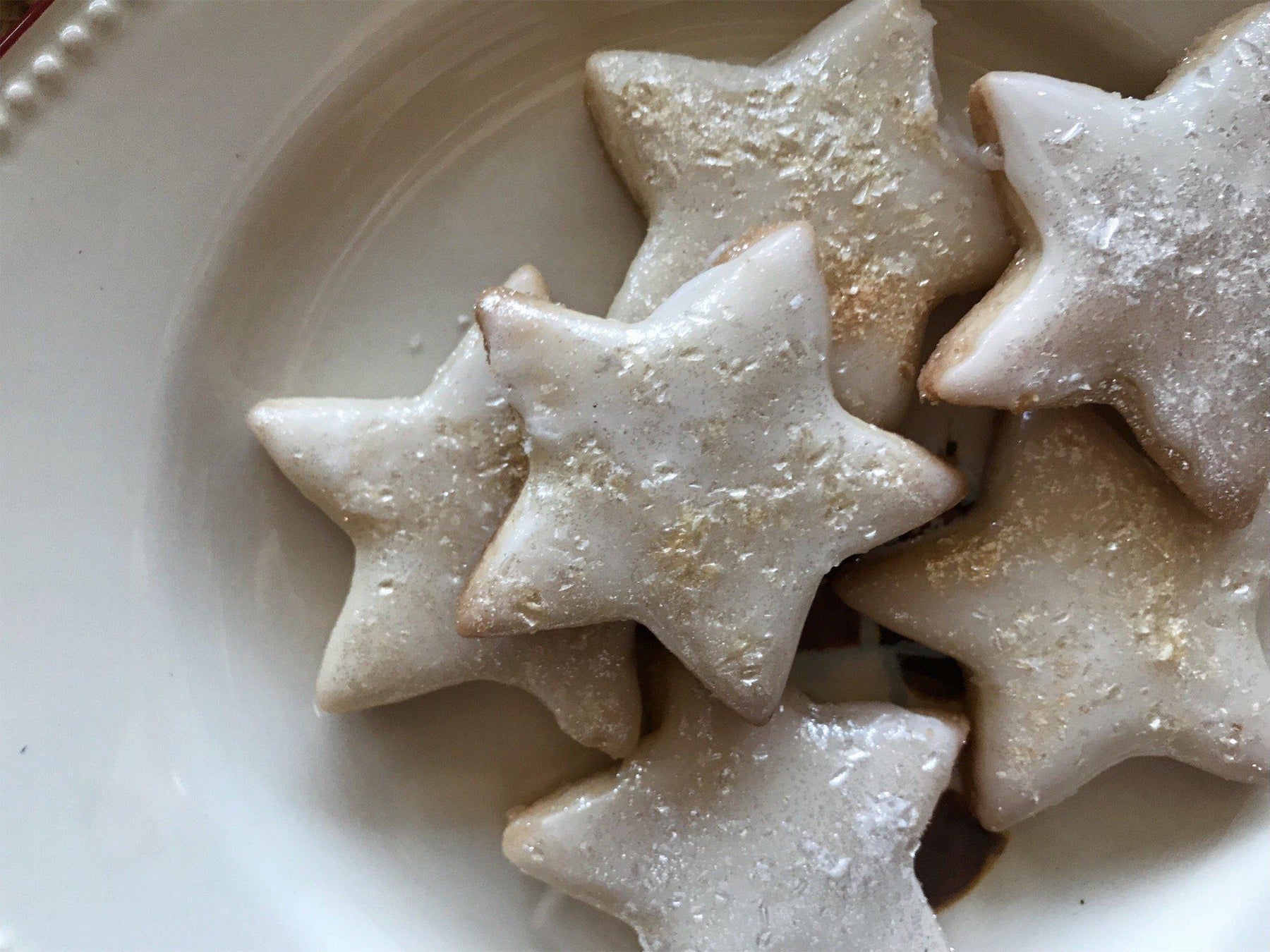 Star-shaped cinnamon cookies with white icing and gold sprinkles on a white plate.