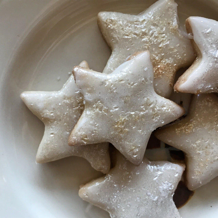 Star-shaped cinnamon cookies with white icing and gold sprinkles on a white plate.