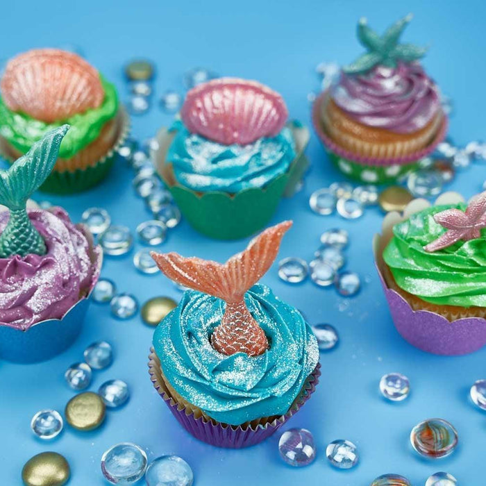 Colorful mermaid cupcakes with shimmering frosting, edible tails, and shells on a blue background with glass beads.